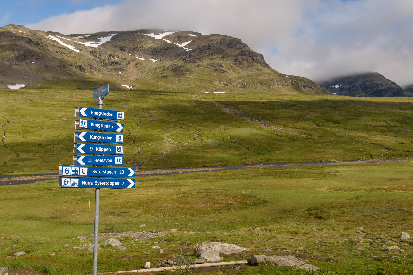 Vy över bergigt landskap, närmast kameran ses en rad skyltar. 